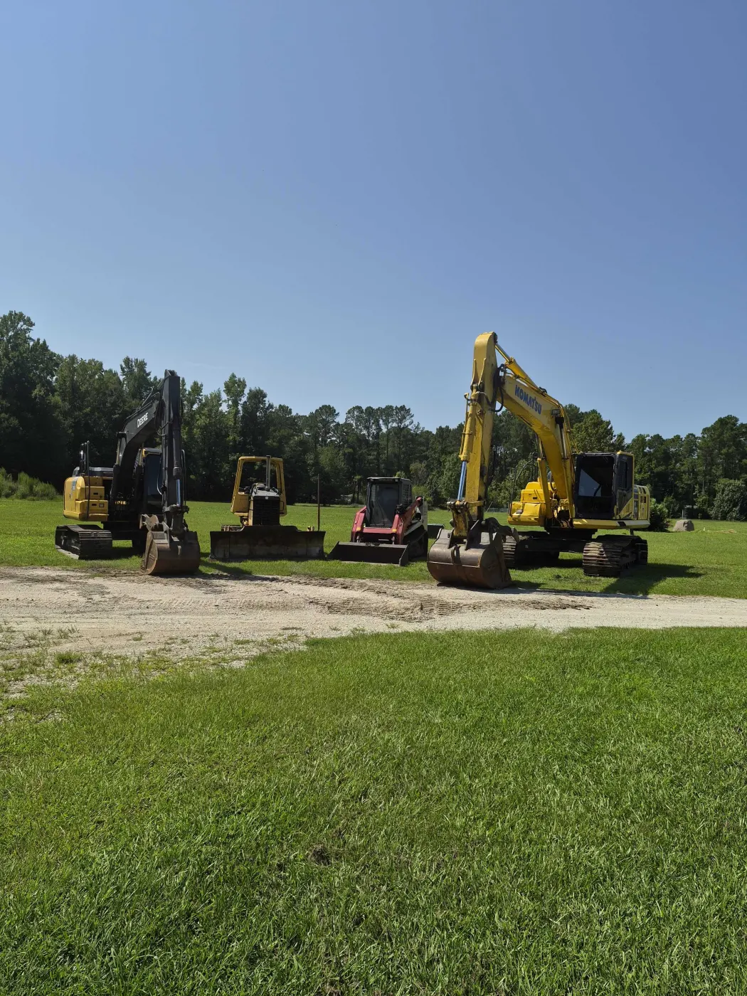 Coastal Brush Mowing excavators and tracked skid steer lined up in a field