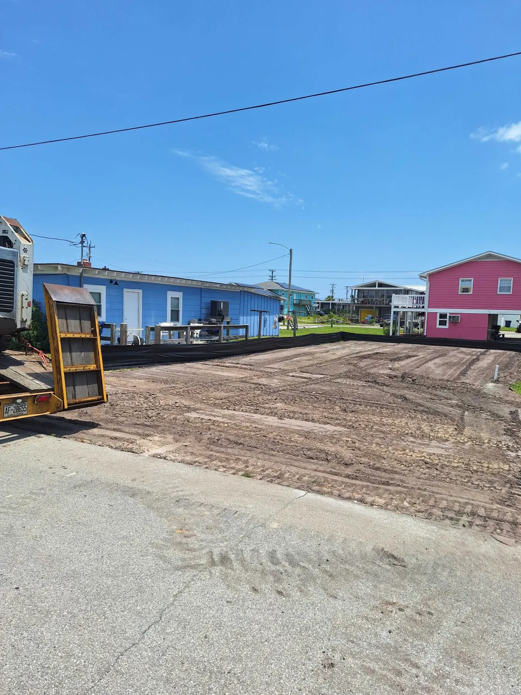 Bare dirt lot graded flat after a demolition near Burgaw, NC, with machine tracks and homes in the background
